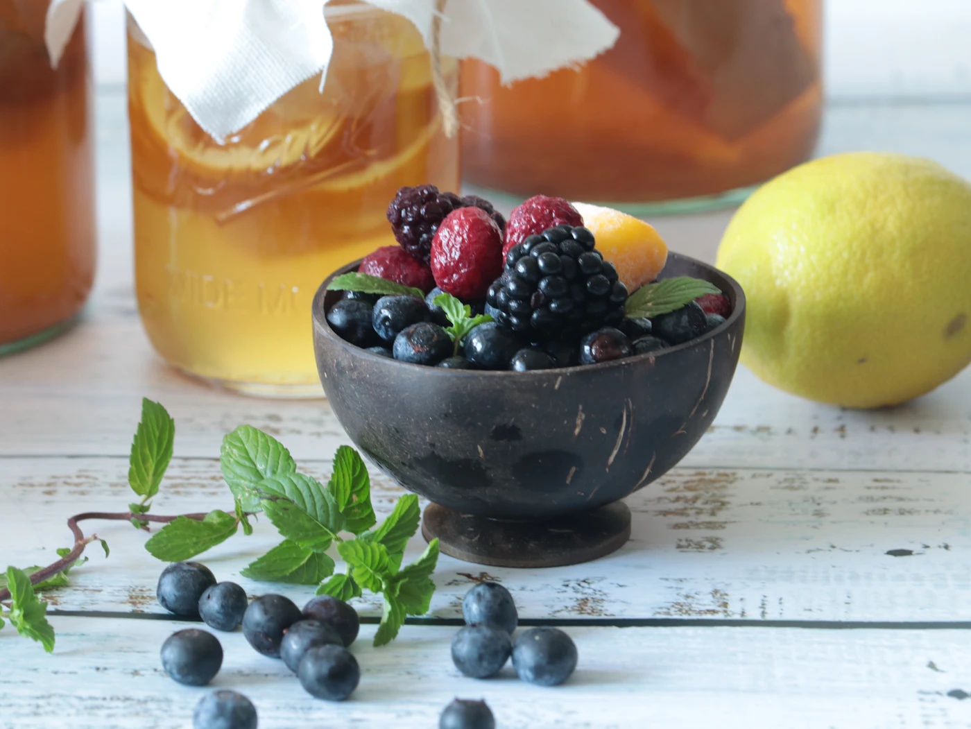 Figs and blueberries in kombucha in a small glass jar, topped with mint