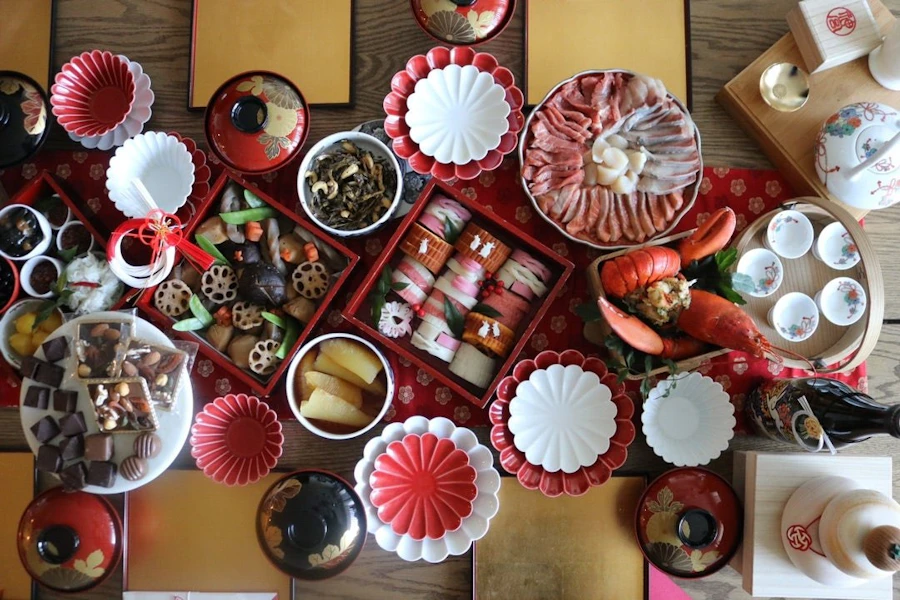 赤と白の器が並ぶお正月の食卓。重箱のおせち、筑前煮、田作り、刺身など