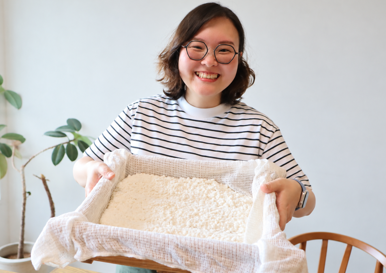 蒸した米に種麹をつけた箱を持つ Joy さん
