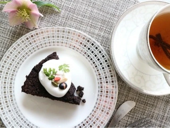 白い皿にのせた、豆乳クリームとエディブルフラワーを飾ったおからのガトーショコラ。バニラビーンズ入りの紅茶を添えて
