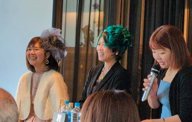 出版記念パーティーで、マイクを持つ司会の方の隣で笑う安藤千英と酒匂ひろ子さん