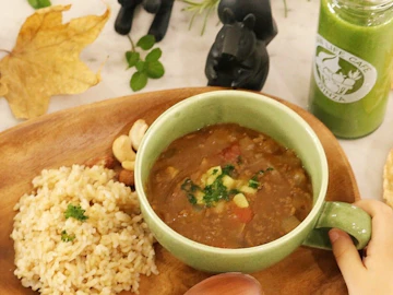 緑のスープカップに入った甘口のひき肉カレーと、木のプレートに盛った玄米ごはん