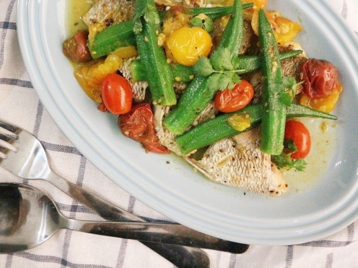 Sea bream acqua pazza on an oval plate with cherry tomatoes, okra and herbs