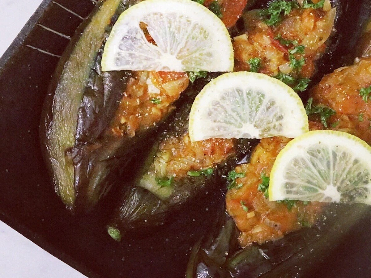 黒い皿に盛った、トマトと玉ねぎを詰めたなすの煮込み。レモンの輪切りとパセリを添えて