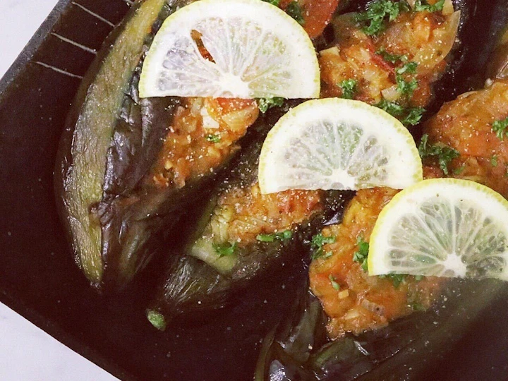 黒い皿に盛った、トマトと玉ねぎを詰めたなすの煮込み。レモンの輪切りとパセリを添えて