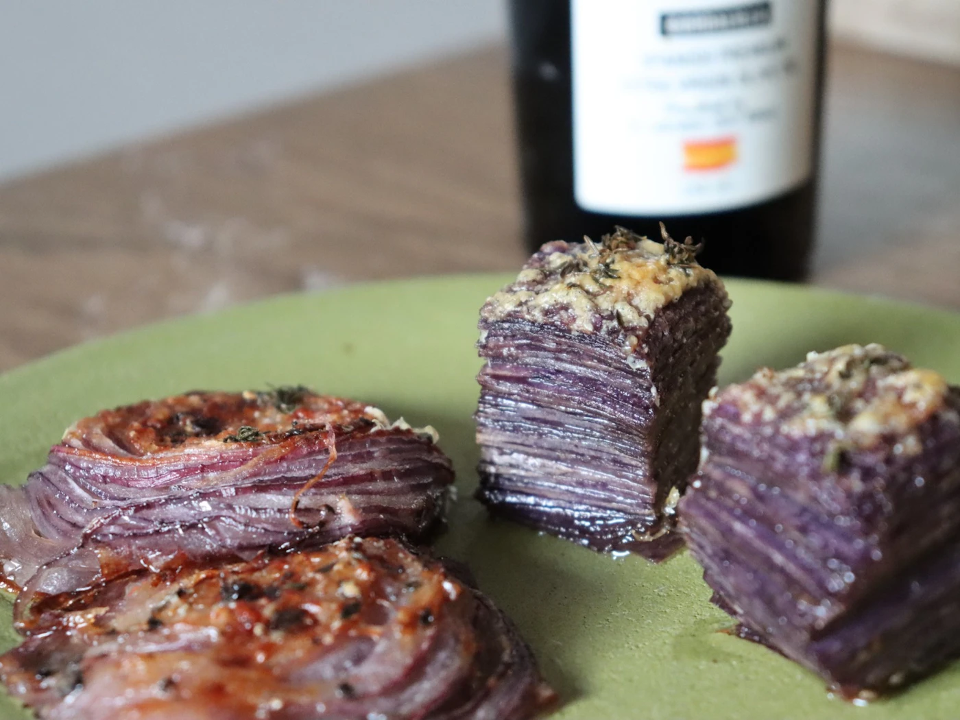Thin layers of purple potato and red onion baked into a millefeuille on a green plate