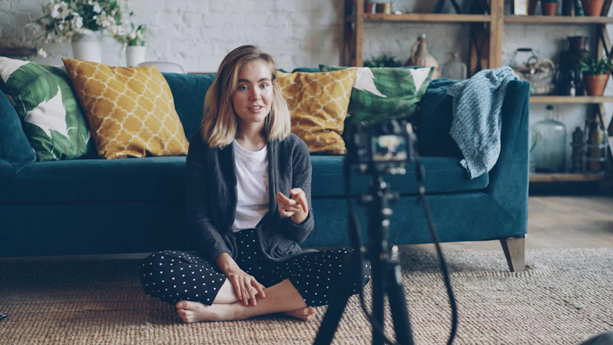 A young woman creating a vlog from her cozy living room with a camera setup.