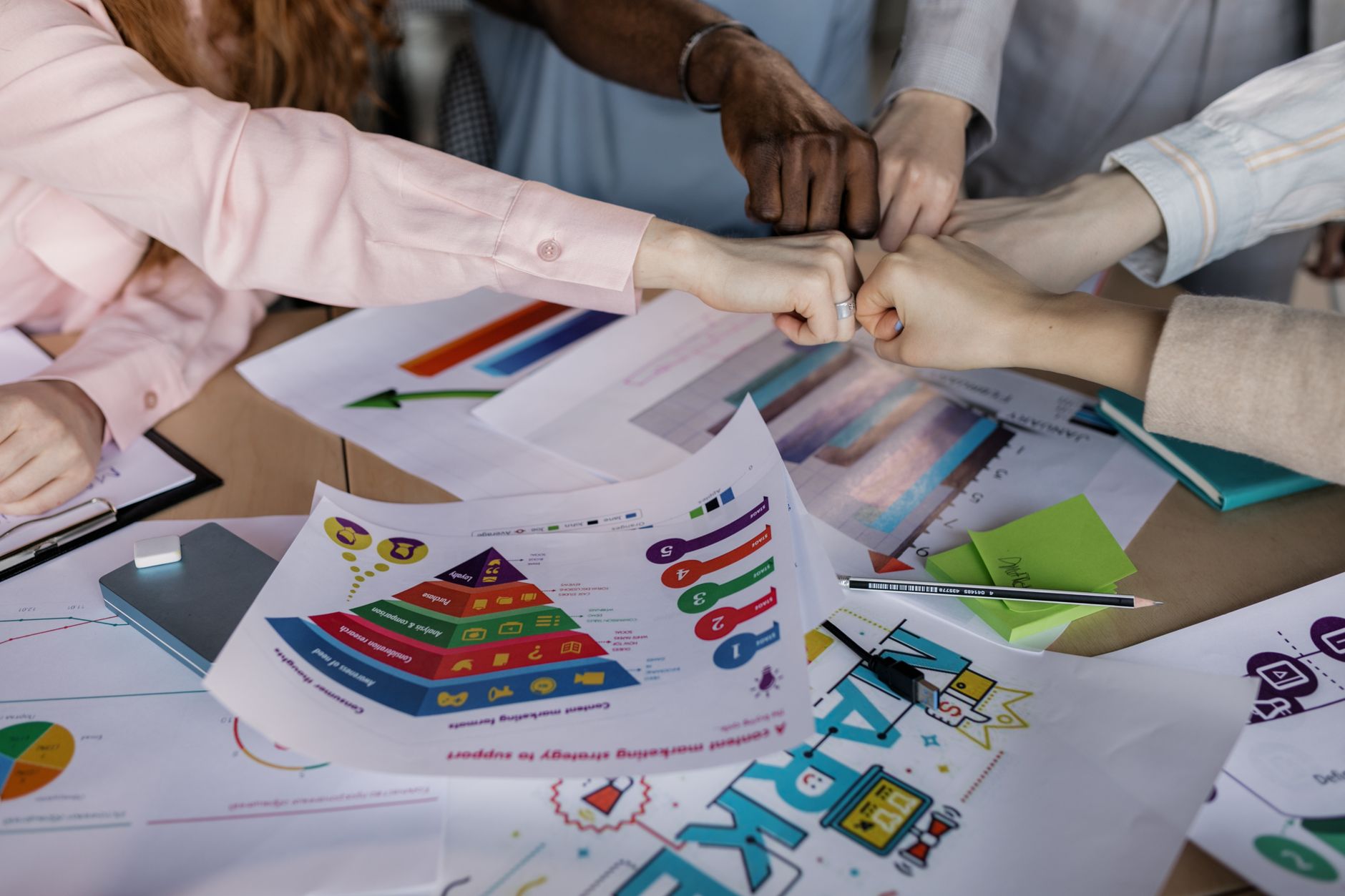 A diverse team unites hands over business reports and marketing strategies, symbolizing teamwork.
