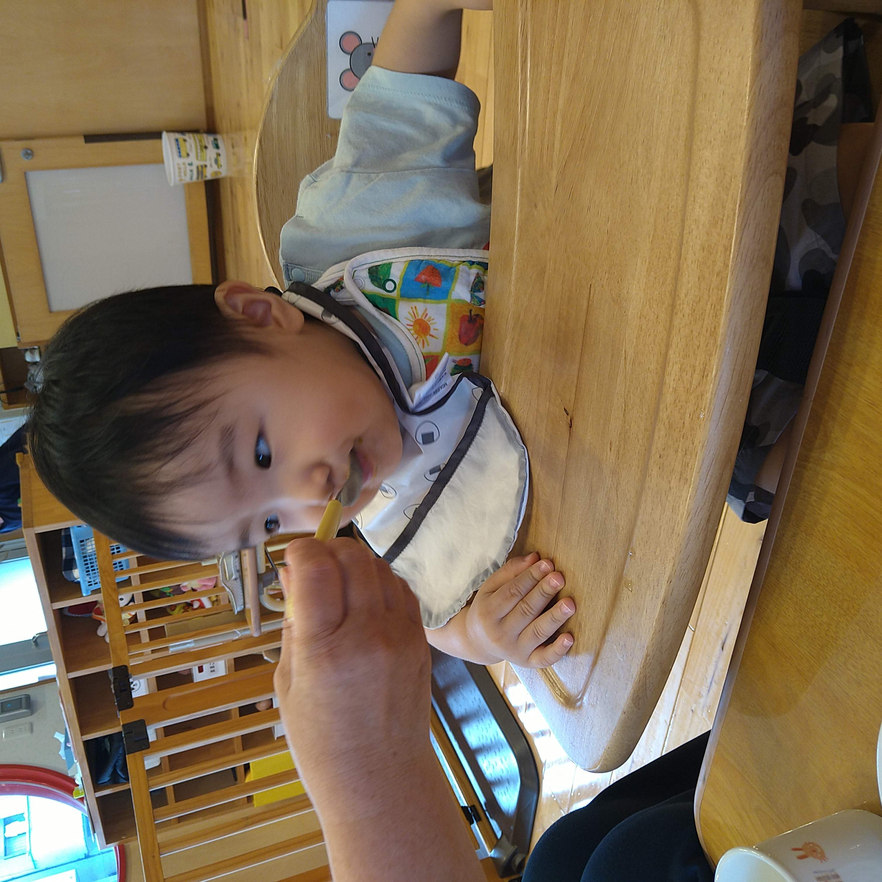 保育士の介助でおやつを一口味わう子ども