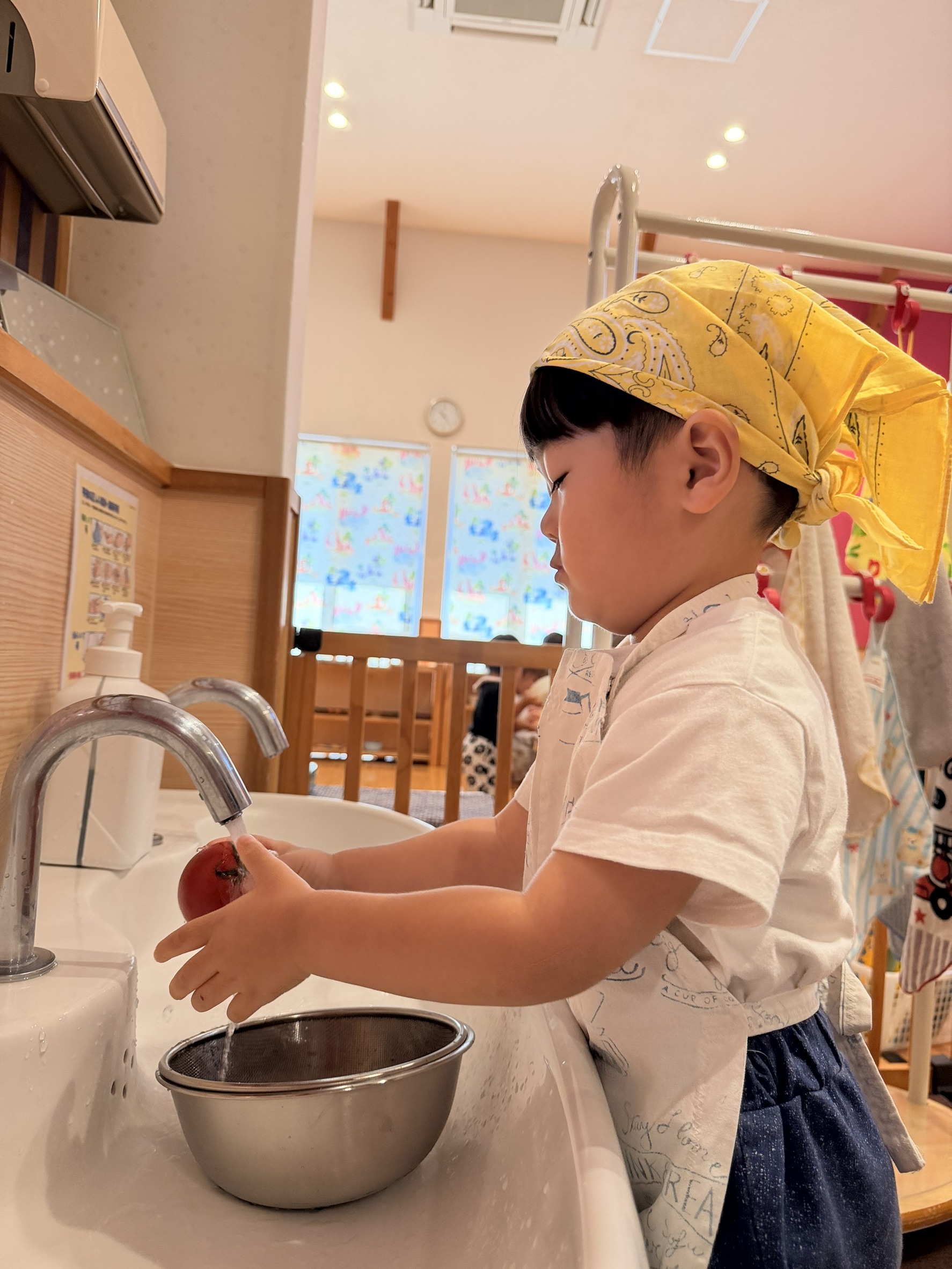 流れる水の下で両手にトマトを持って洗う子ども