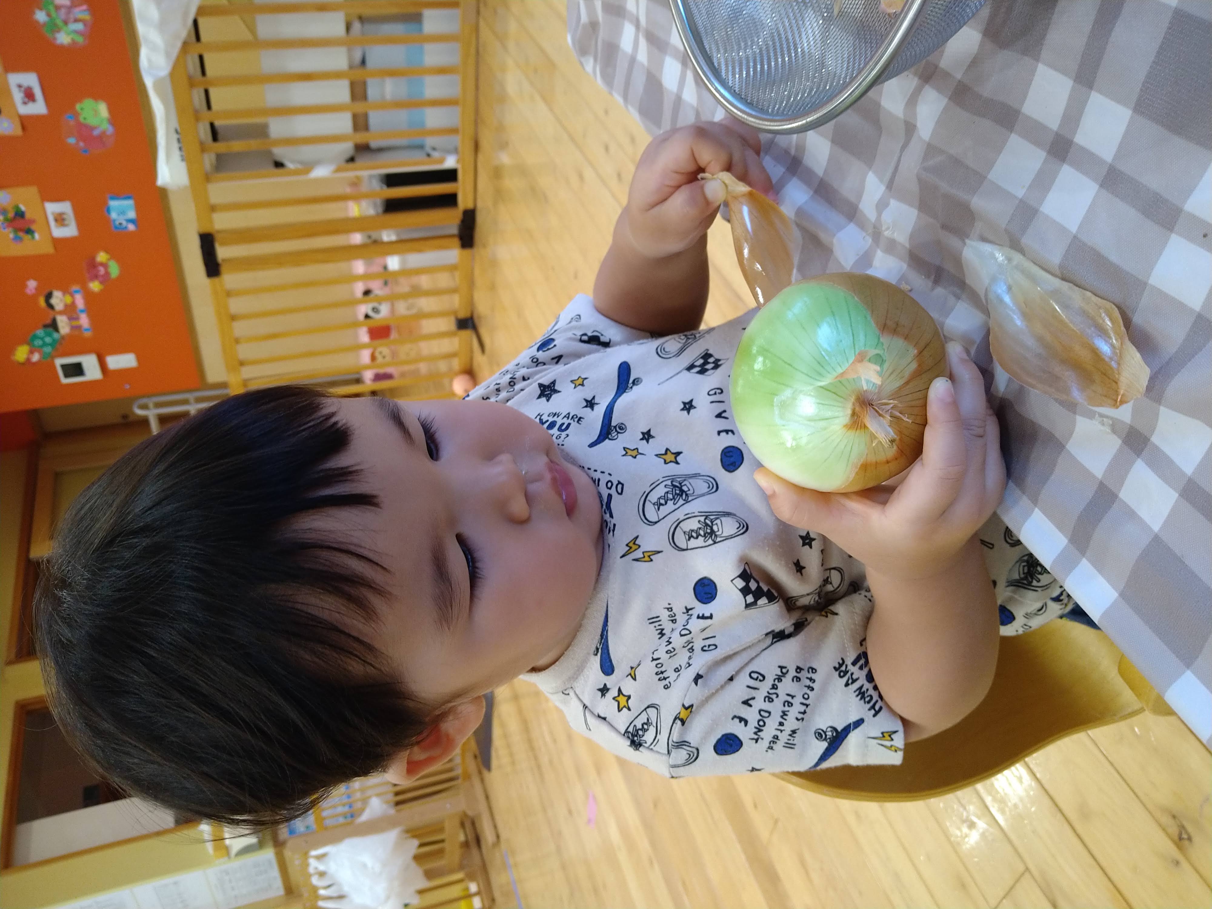 玉ねぎを支えながら皮の端をつまむ子ども