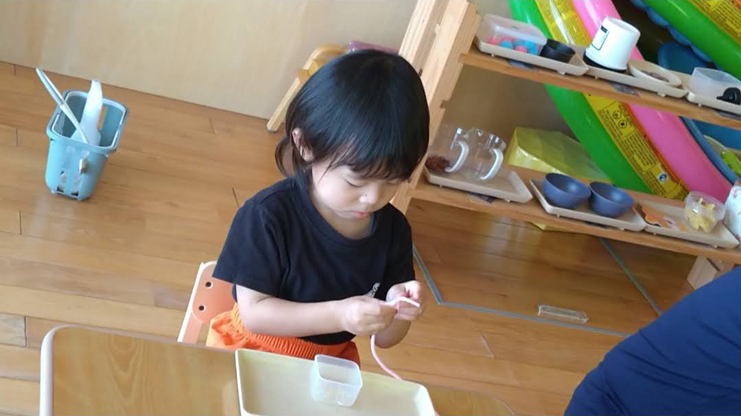 トレーの前で紐通しに集中して取り組む子ども