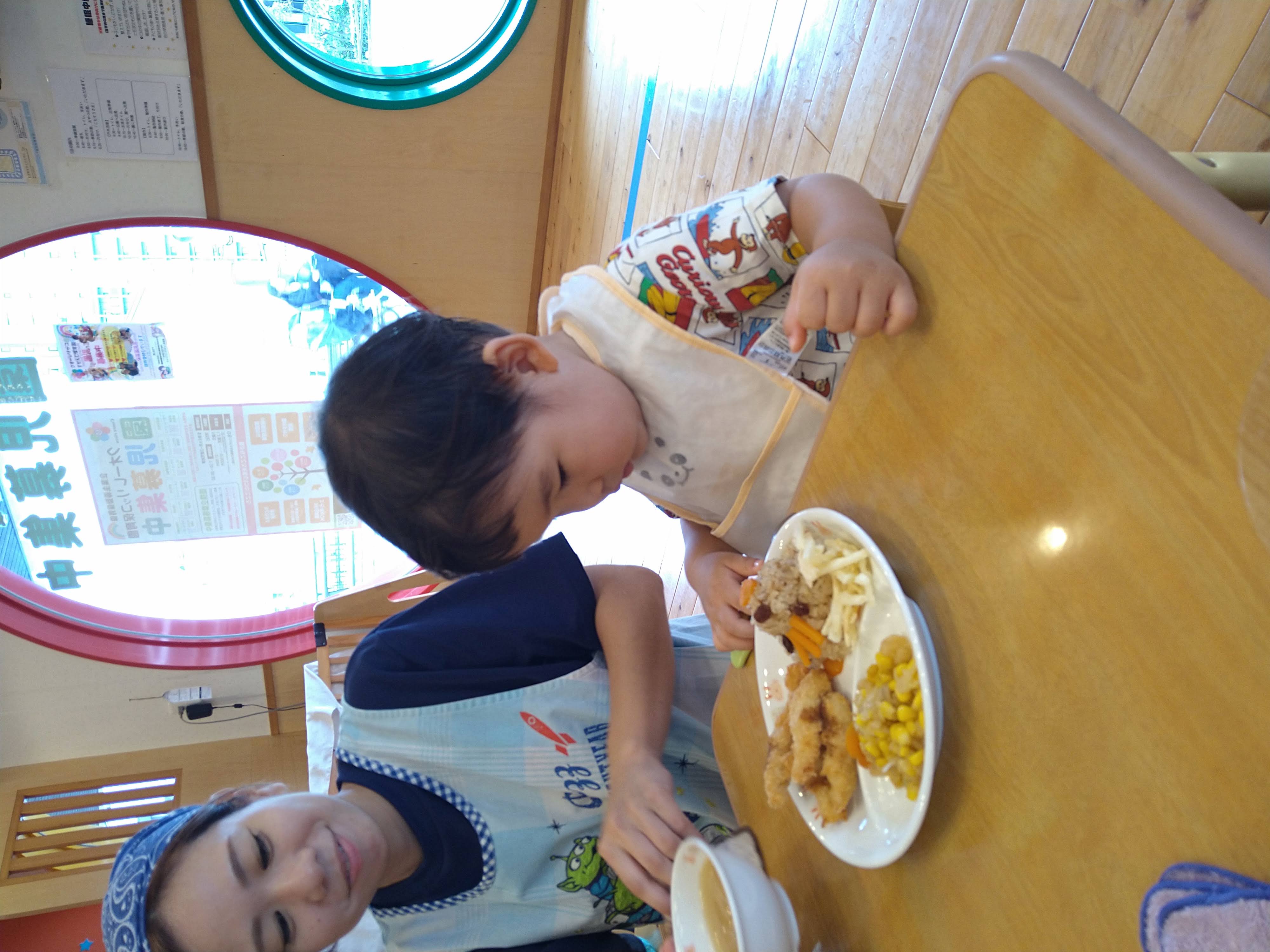 保育士に見守られながら皿へ手を伸ばす子ども