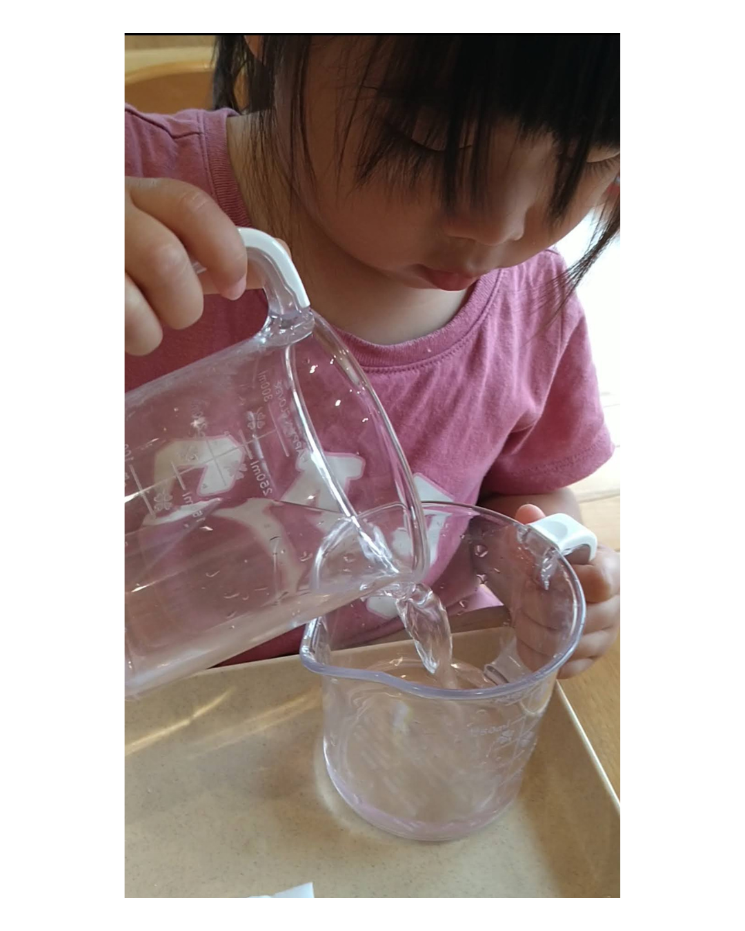 透明な容器を両手で支えて水をあけうつす子ども