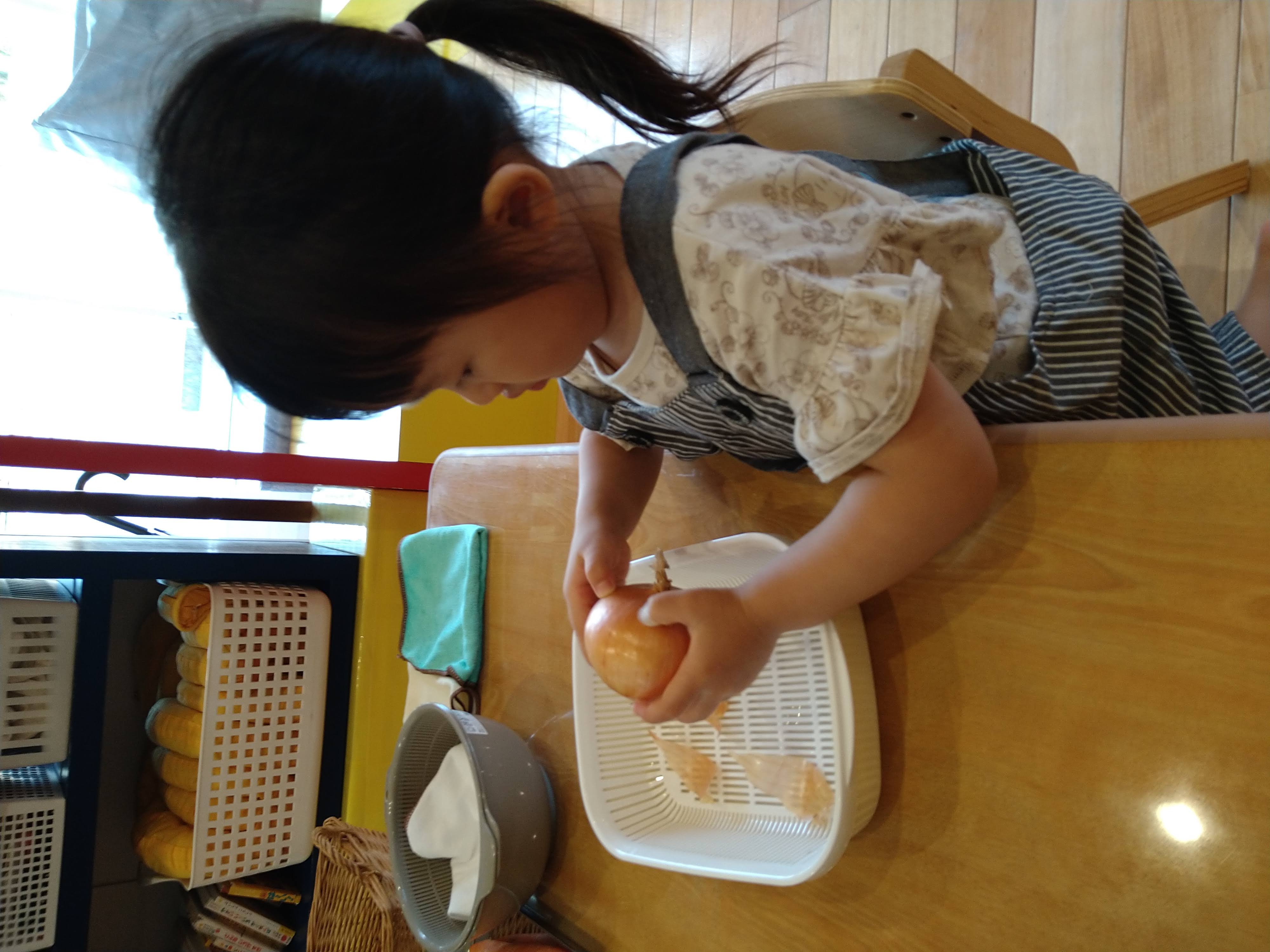 玉ねぎを両手で持ち皮の端を探す子ども