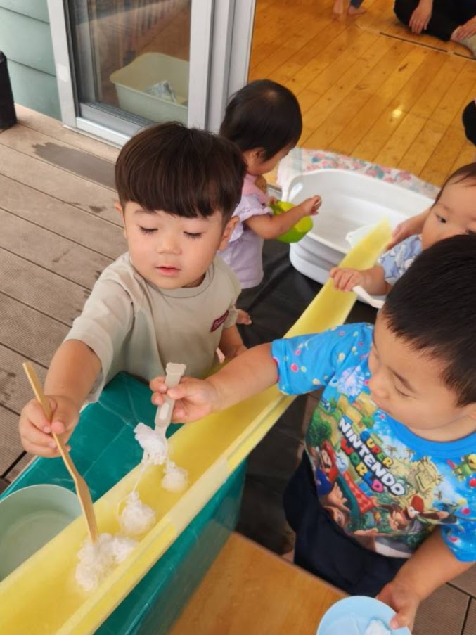そうめん流しで流れてくるそうめんを道具ですくう子どもたち