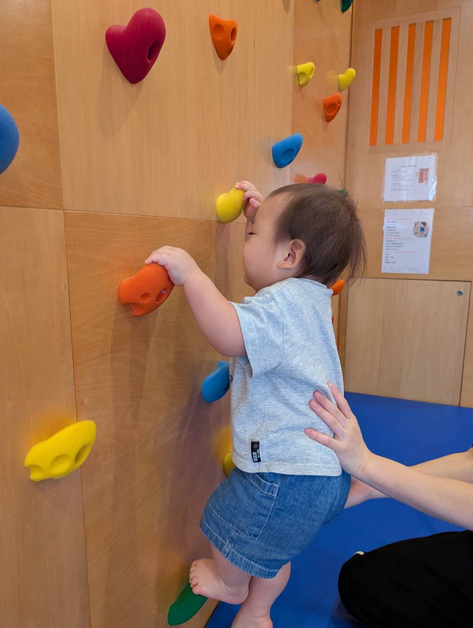保育士に支えられながらホールドへ手を伸ばす子ども