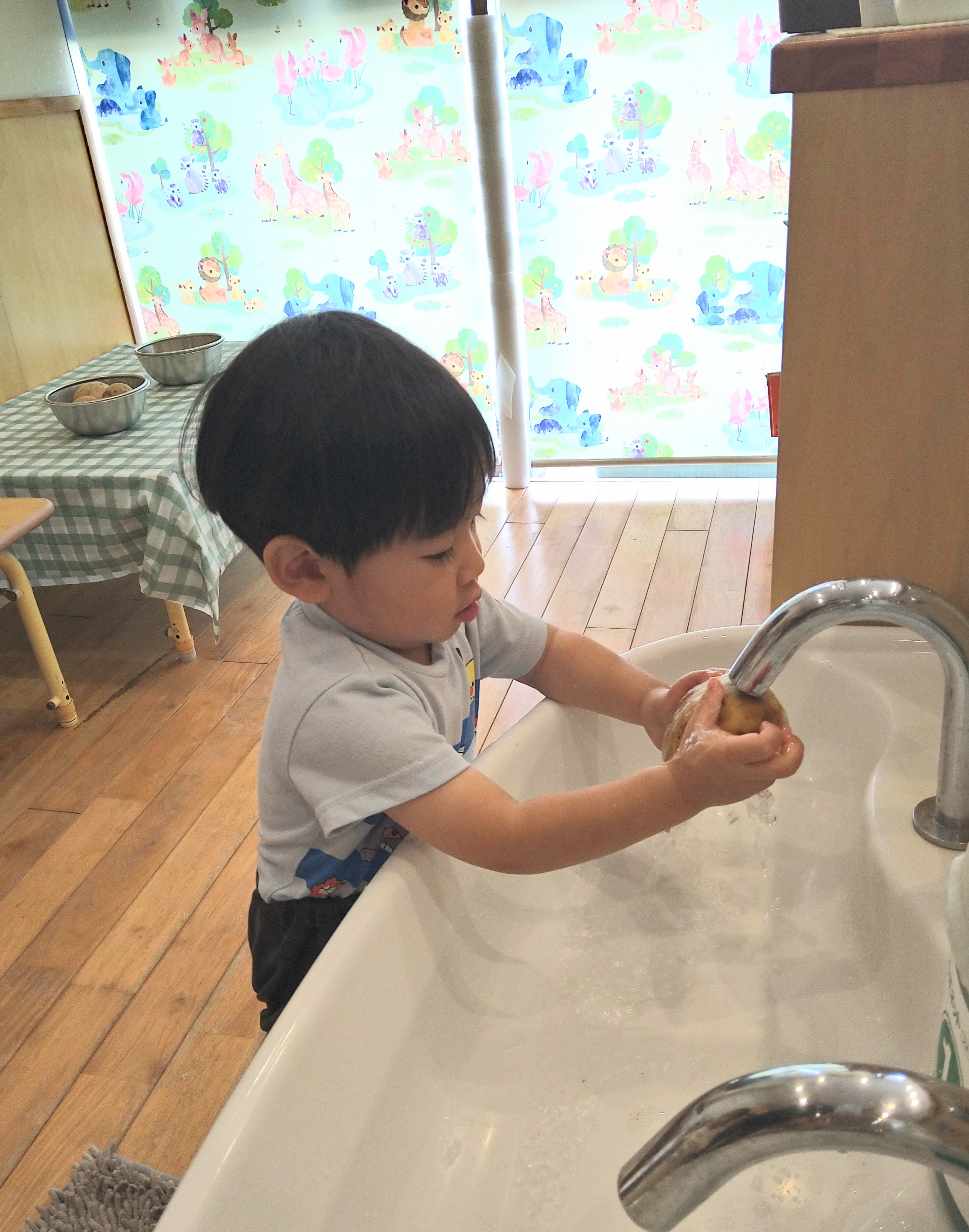 水道でじゃがいもを両手に持って洗う子ども
