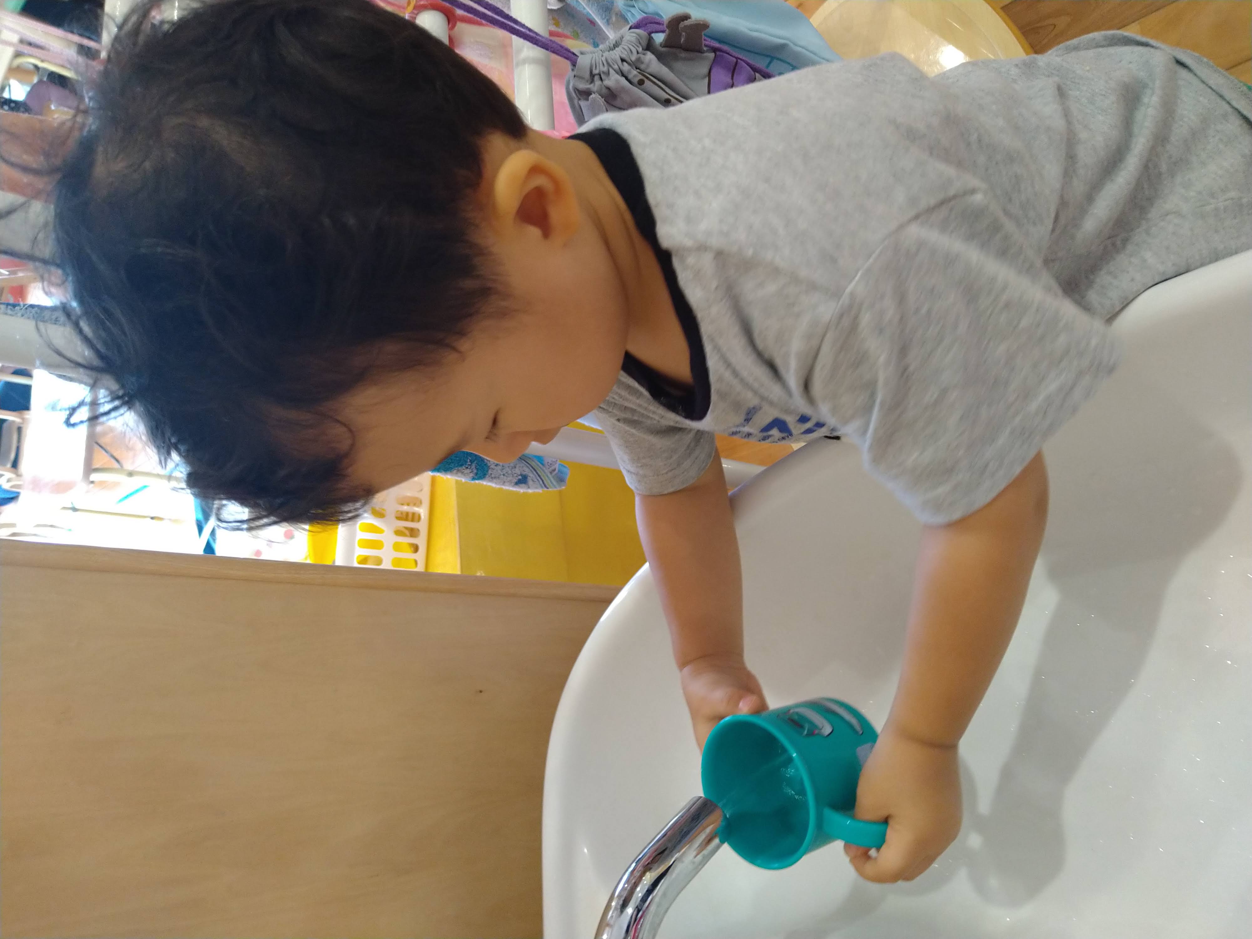 両手でコップを支えて水を入れる子ども
