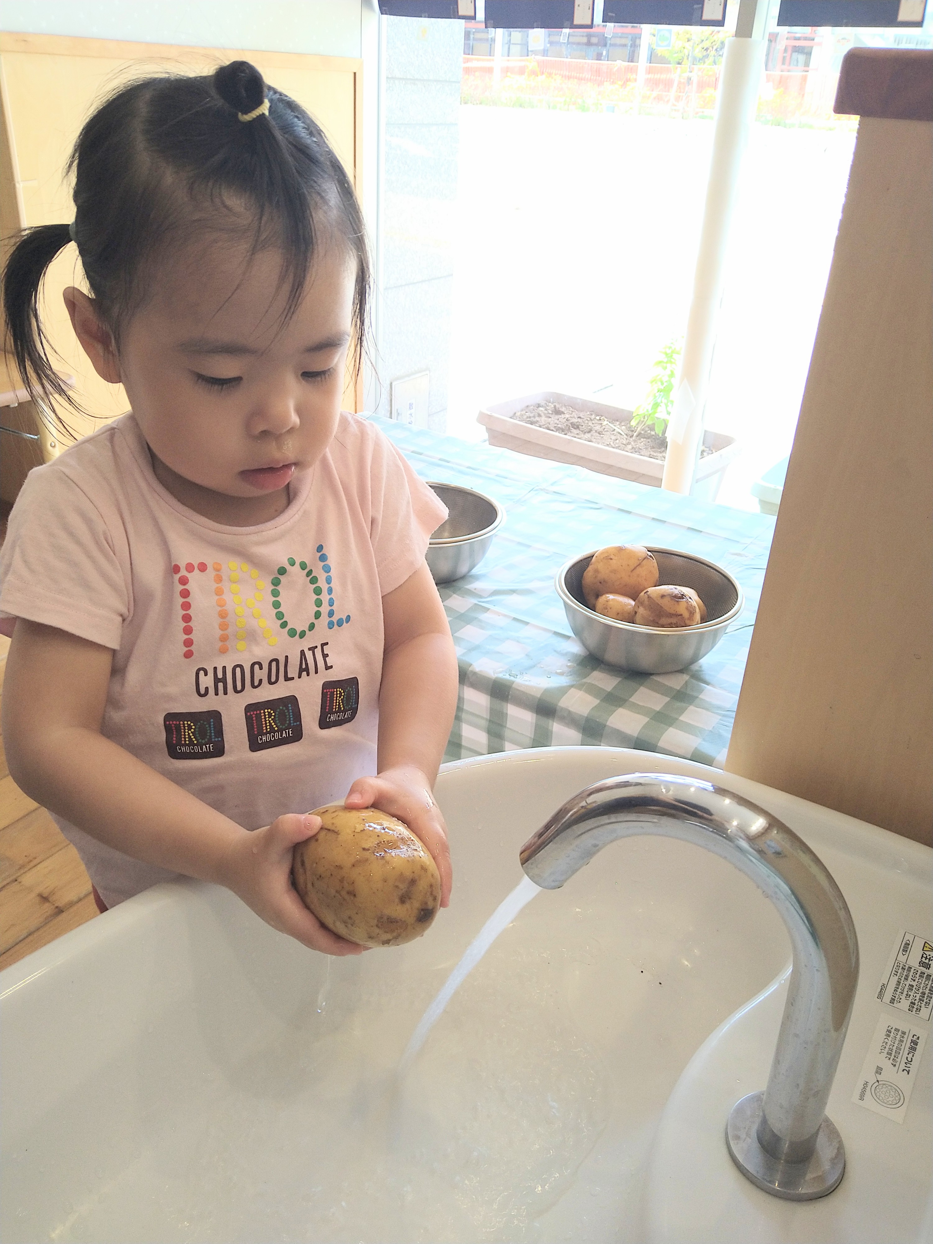 洗ったじゃがいもを両手で持ち仕上がりを確かめる子ども