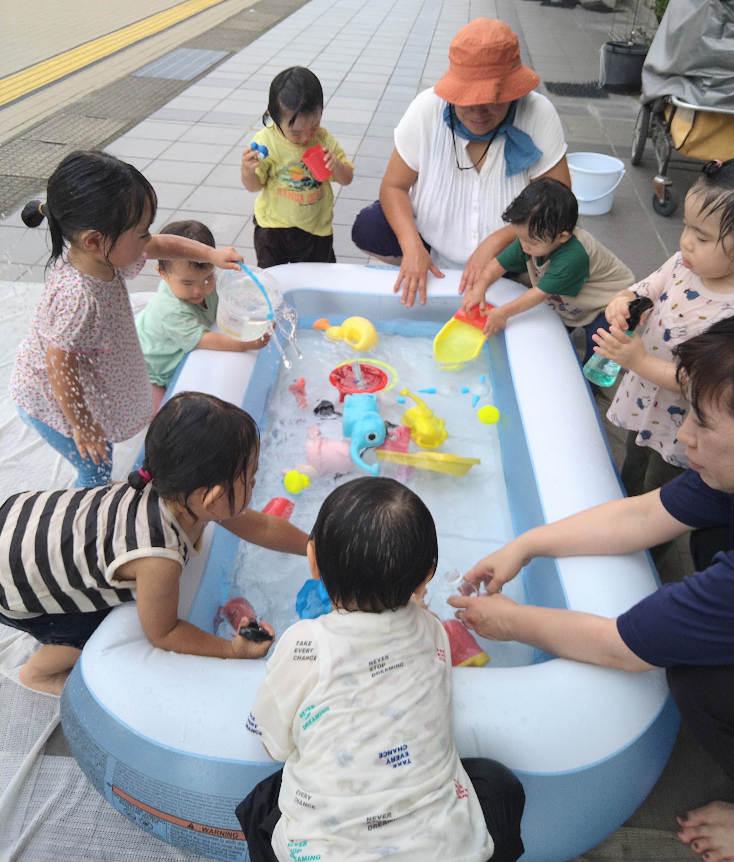 友だちとたらいを囲み、カップやじょうろで遊ぶ様子