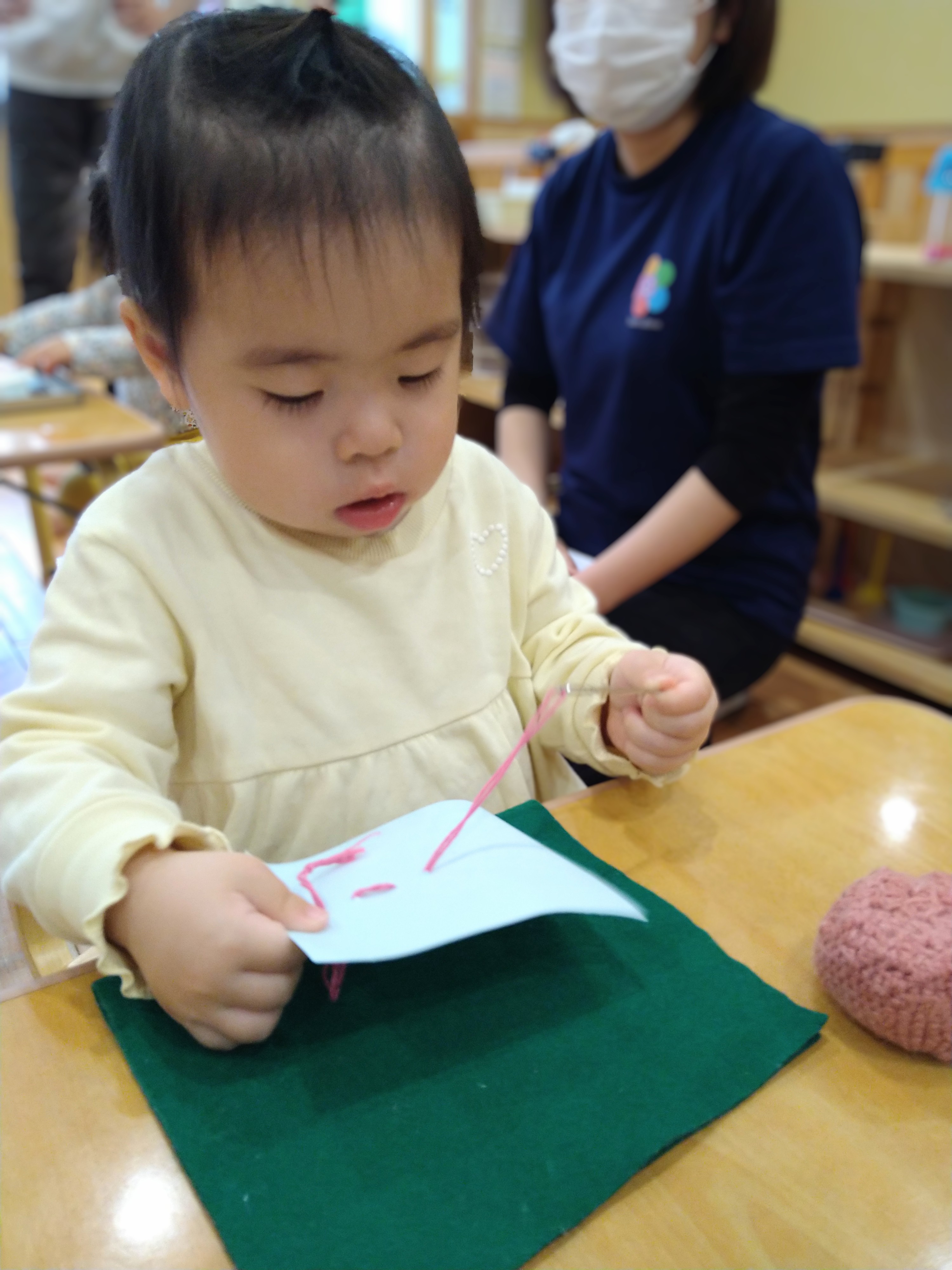 台紙の穴へひもを通そうと集中する子ども