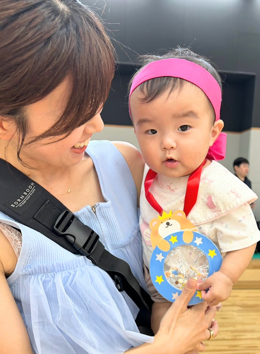 赤いはちまきを着け保護者に抱かれてくまのメダルを持つ子ども