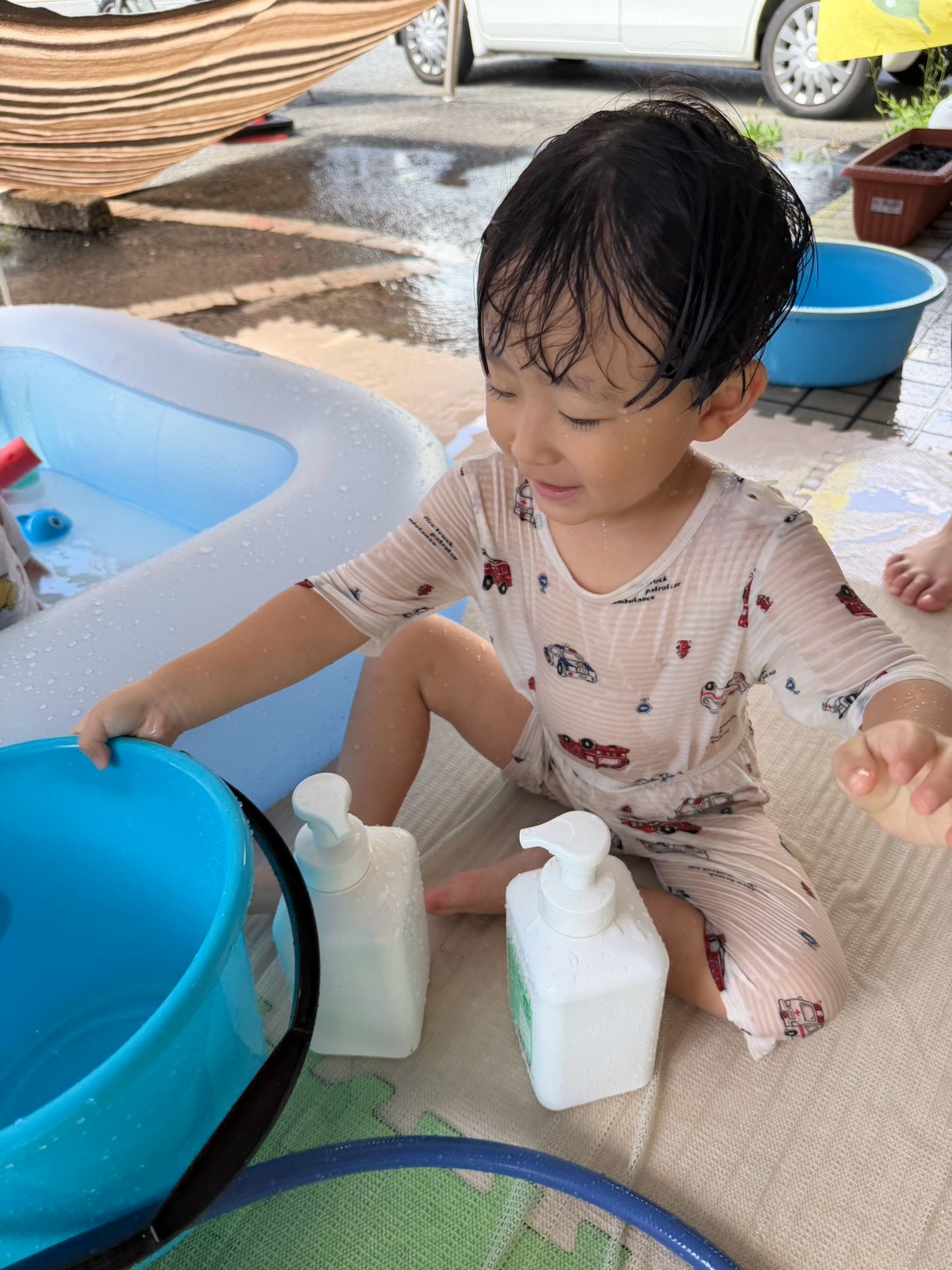 バケツや容器に手を伸ばして水遊びを試す子ども