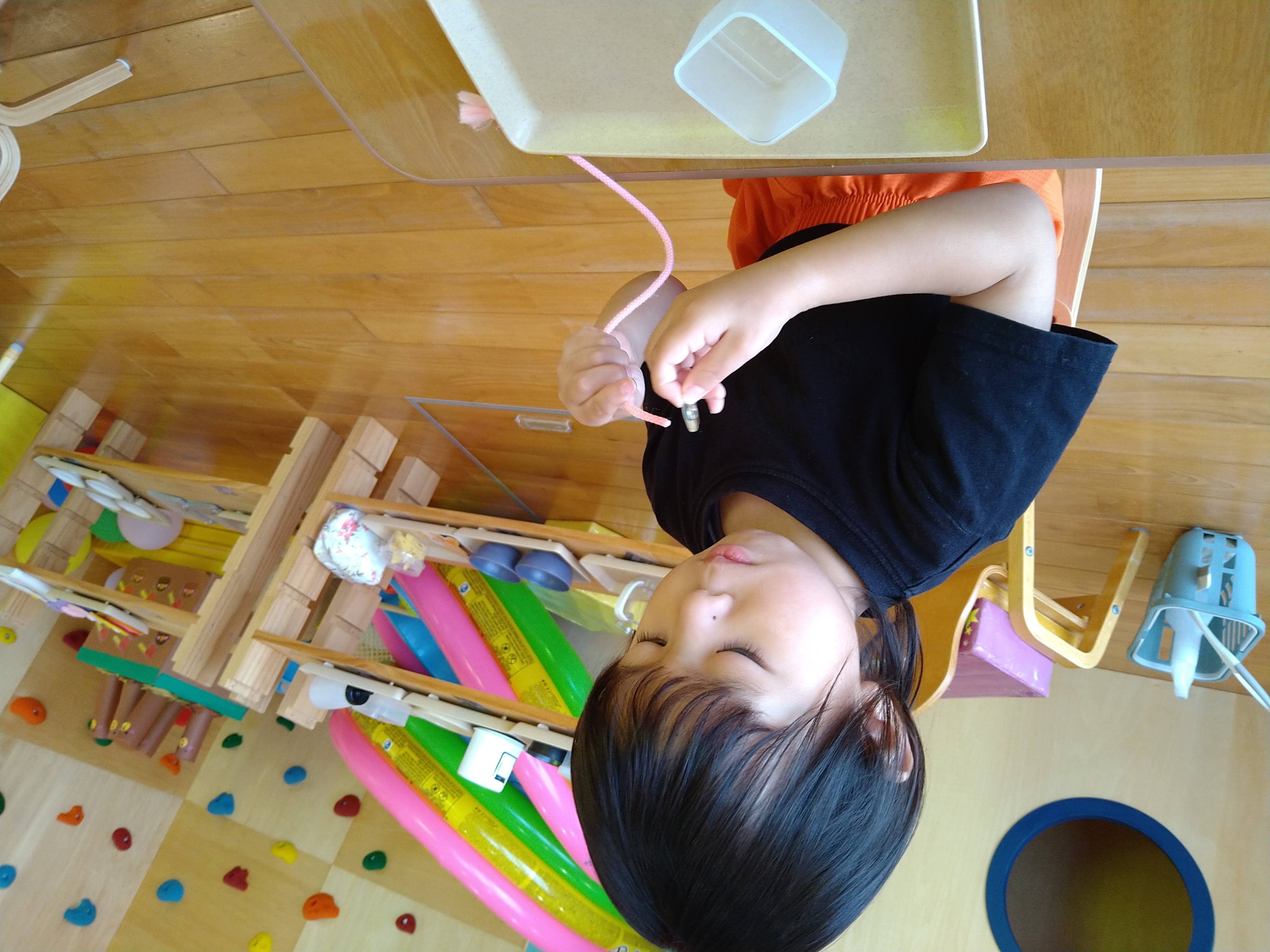 紐の先とパーツを両手で持ち通す位置を確かめる子ども