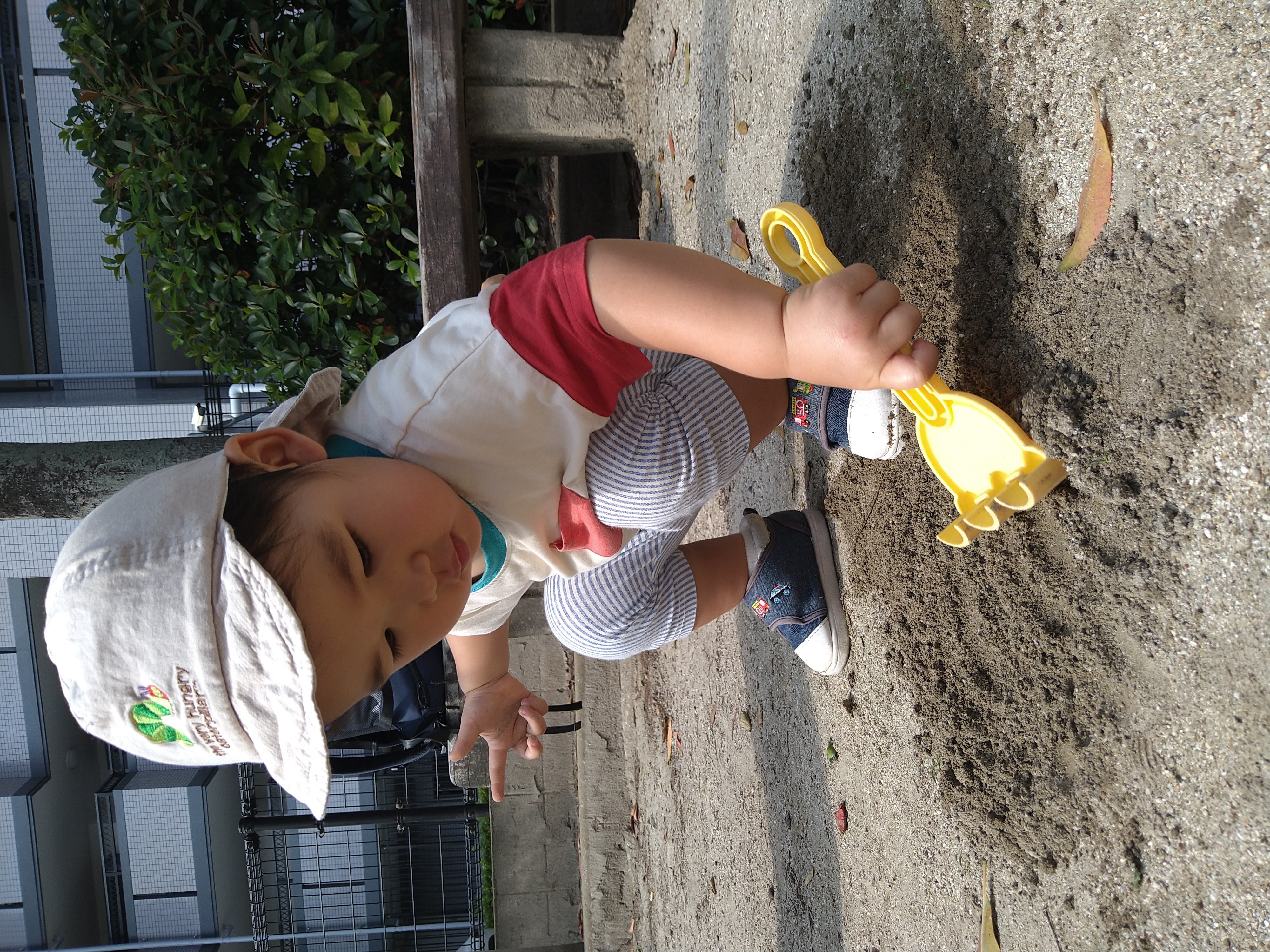 黄色いスコップを握って砂をすくおうとする子ども