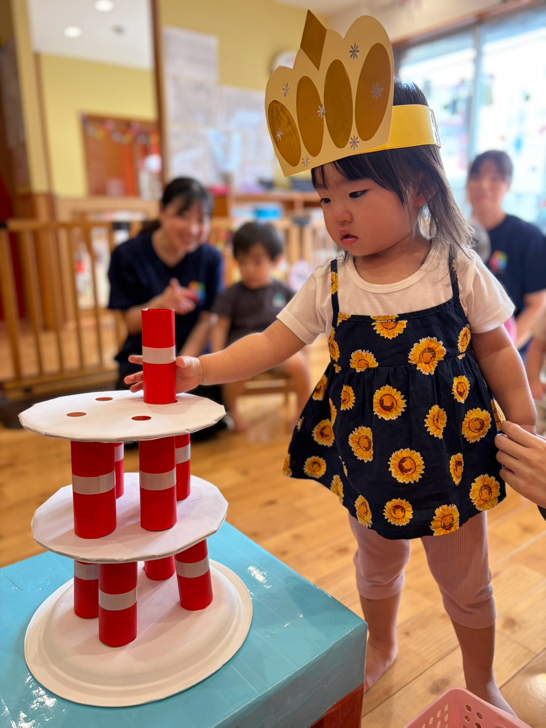 お誕生日会で冠をつけ筒を積み重ねる子ども