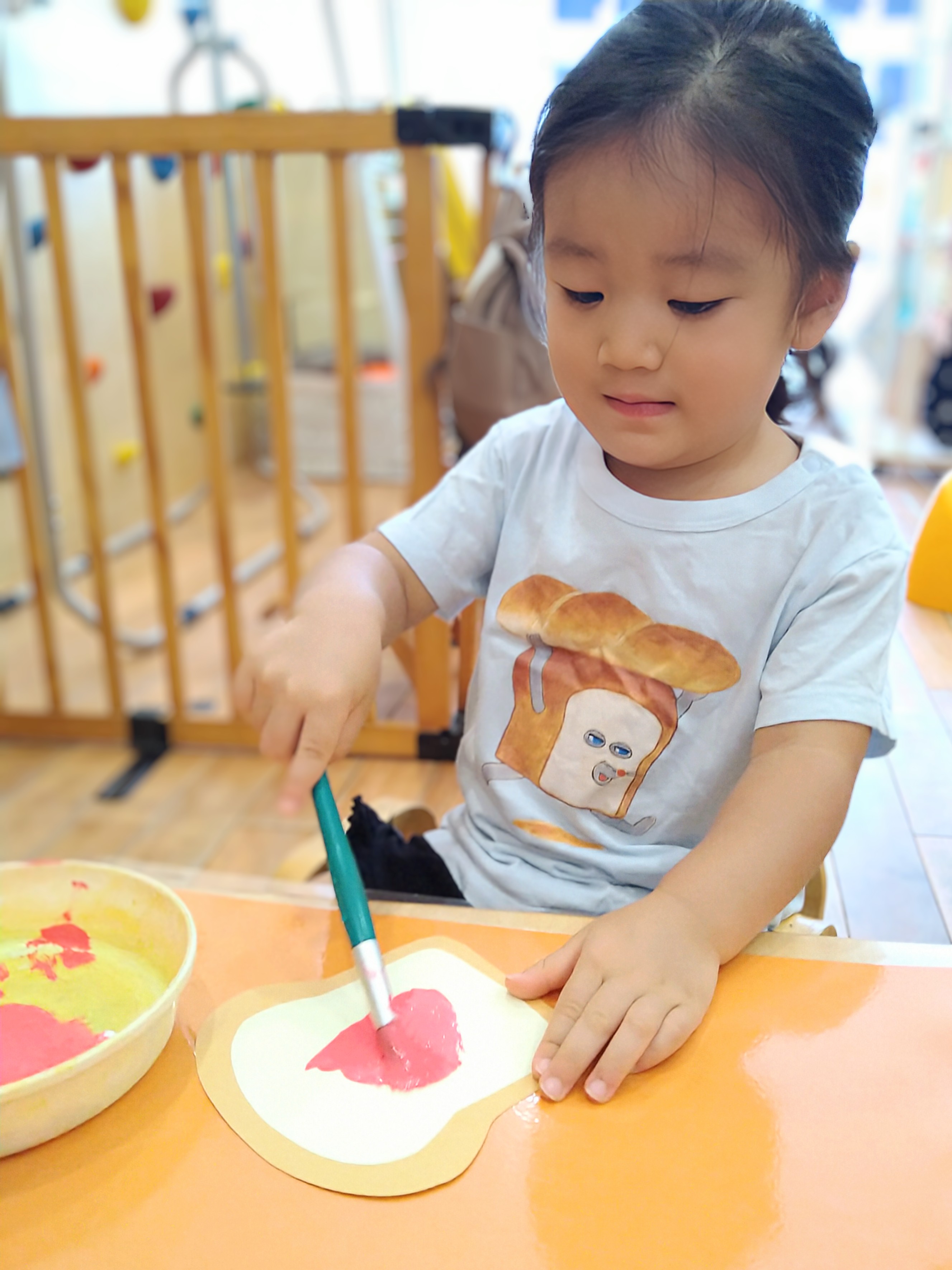 筆でパン形の台紙へ赤い絵の具を塗る子ども