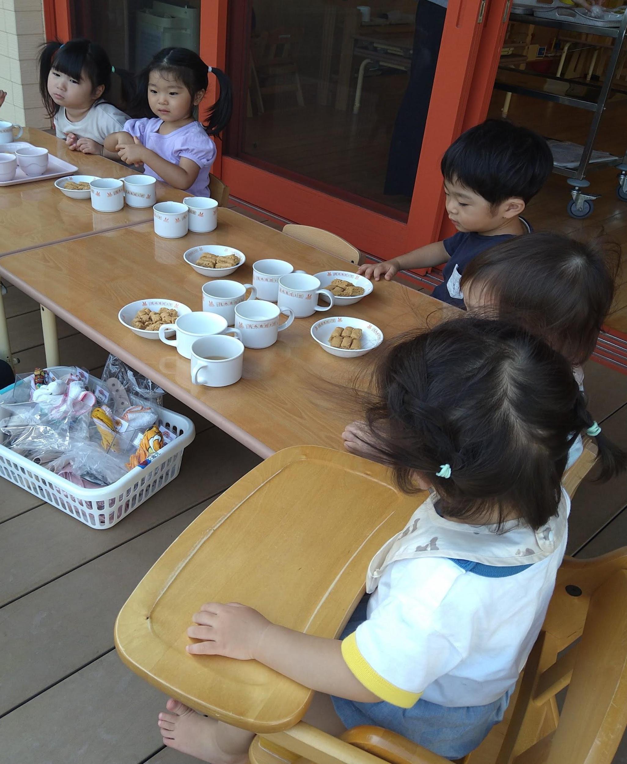 テラスのテーブルを囲んでおやつを待つ子どもたち
