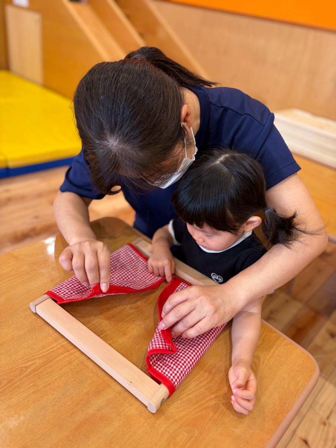 保育士と一緒に着衣枠のチャックの動きを見る子ども