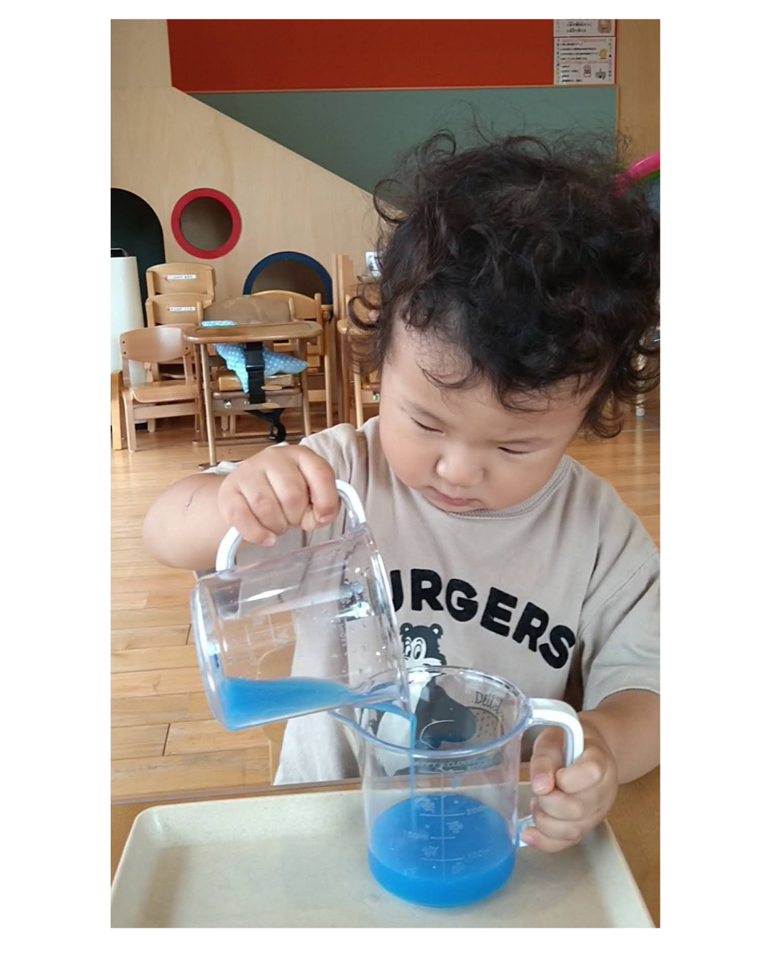 青い水を別の容器へ注ぎ終えるまで見つめる子ども