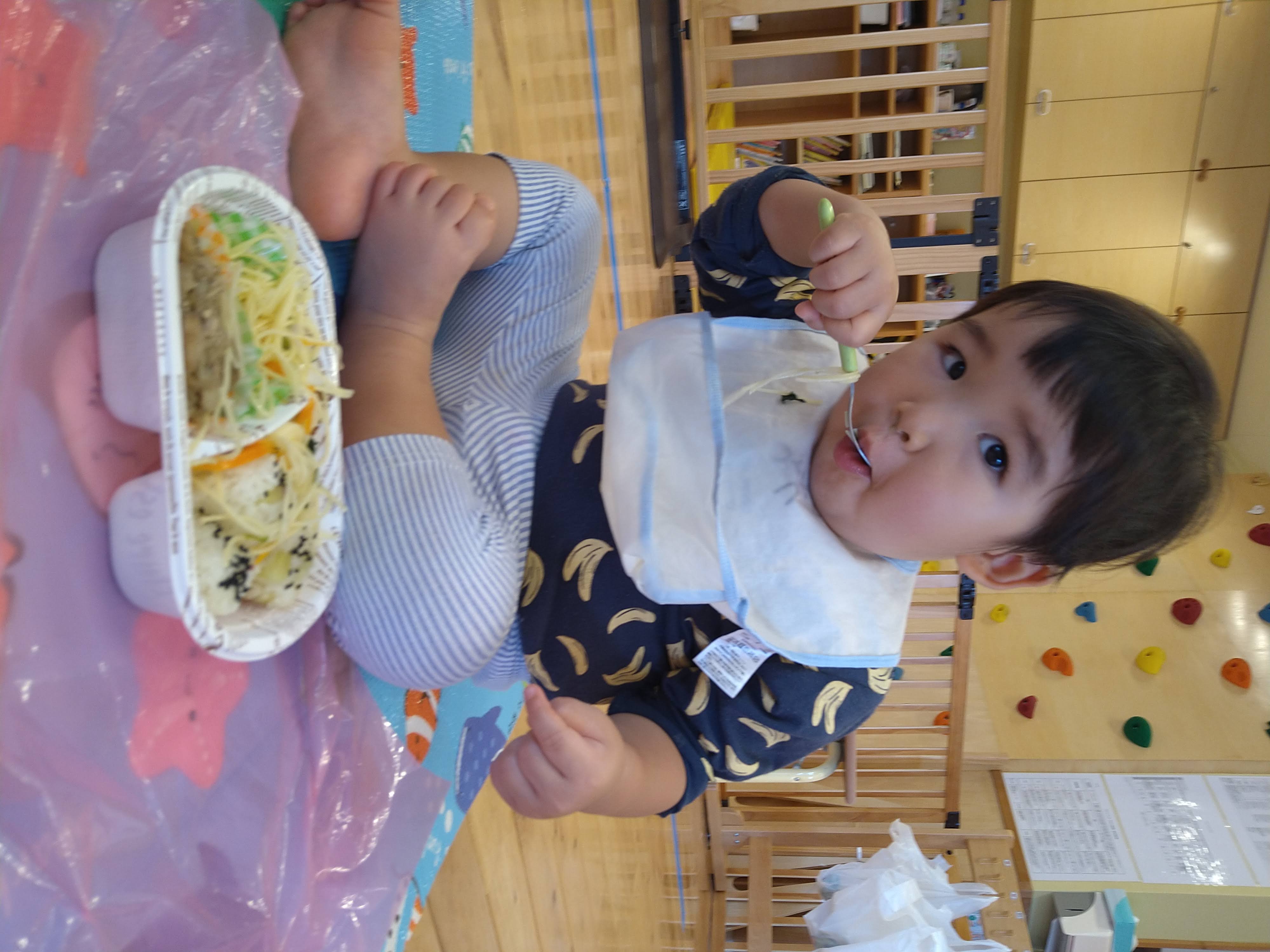 給食を前にスプーンを口へ運ぶ子ども