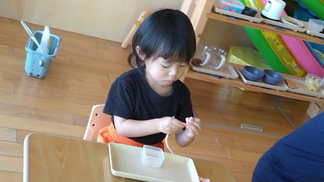 紐をつまみ両手を使って引き出す子ども