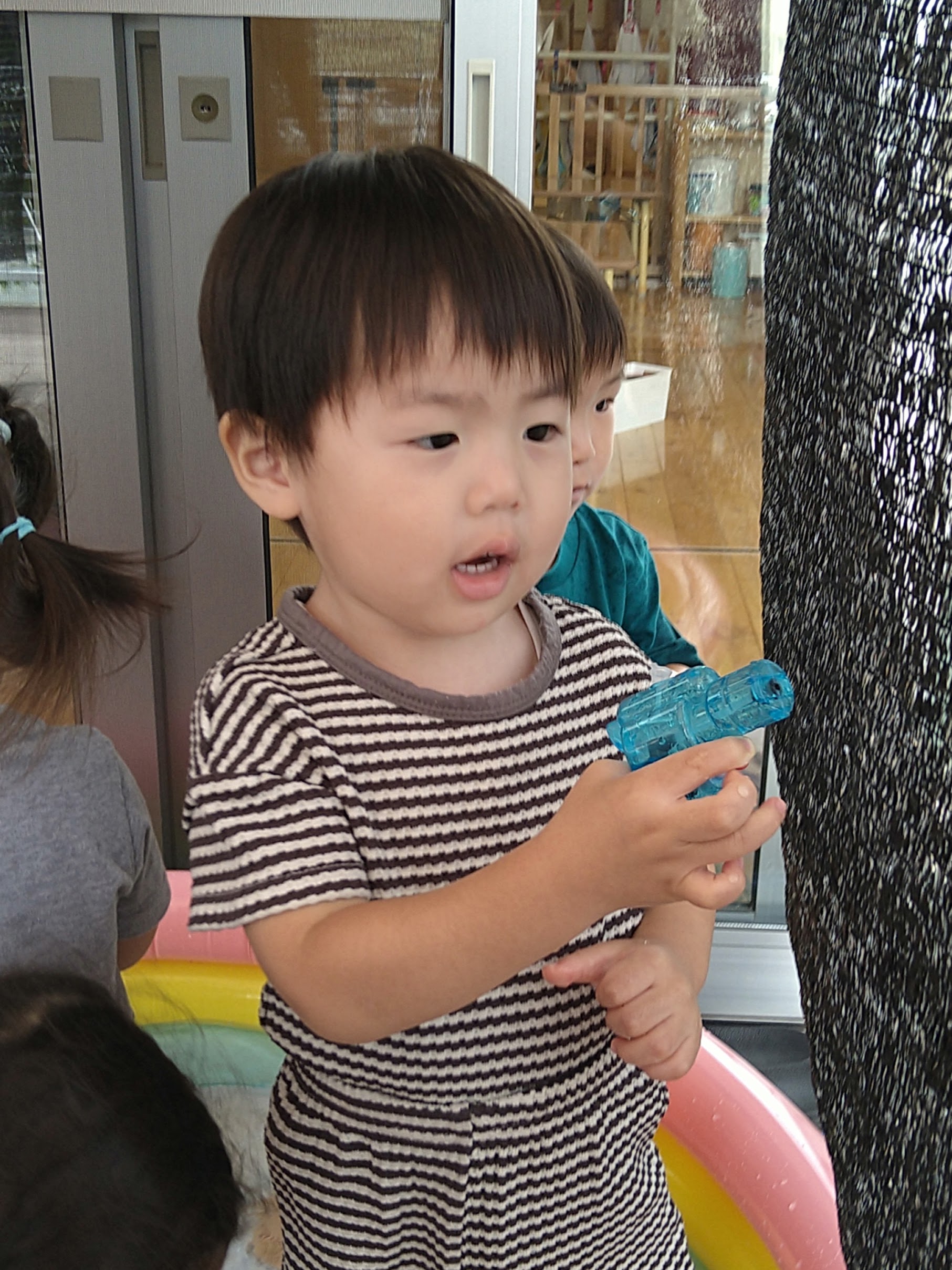水遊びで青い容器を両手に持ち確かめる子ども