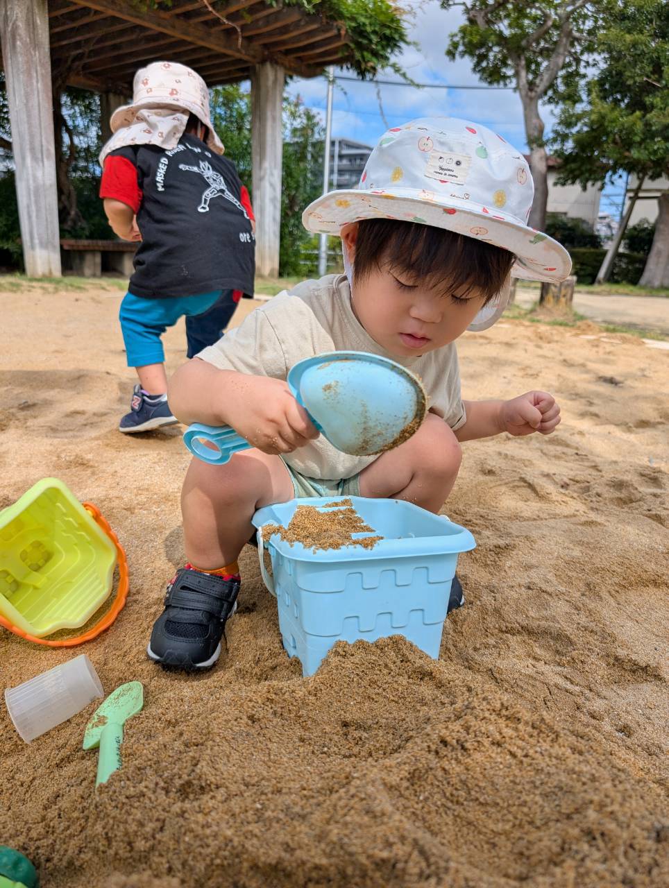 バケツへ砂を入れながら手元を見つめる子ども