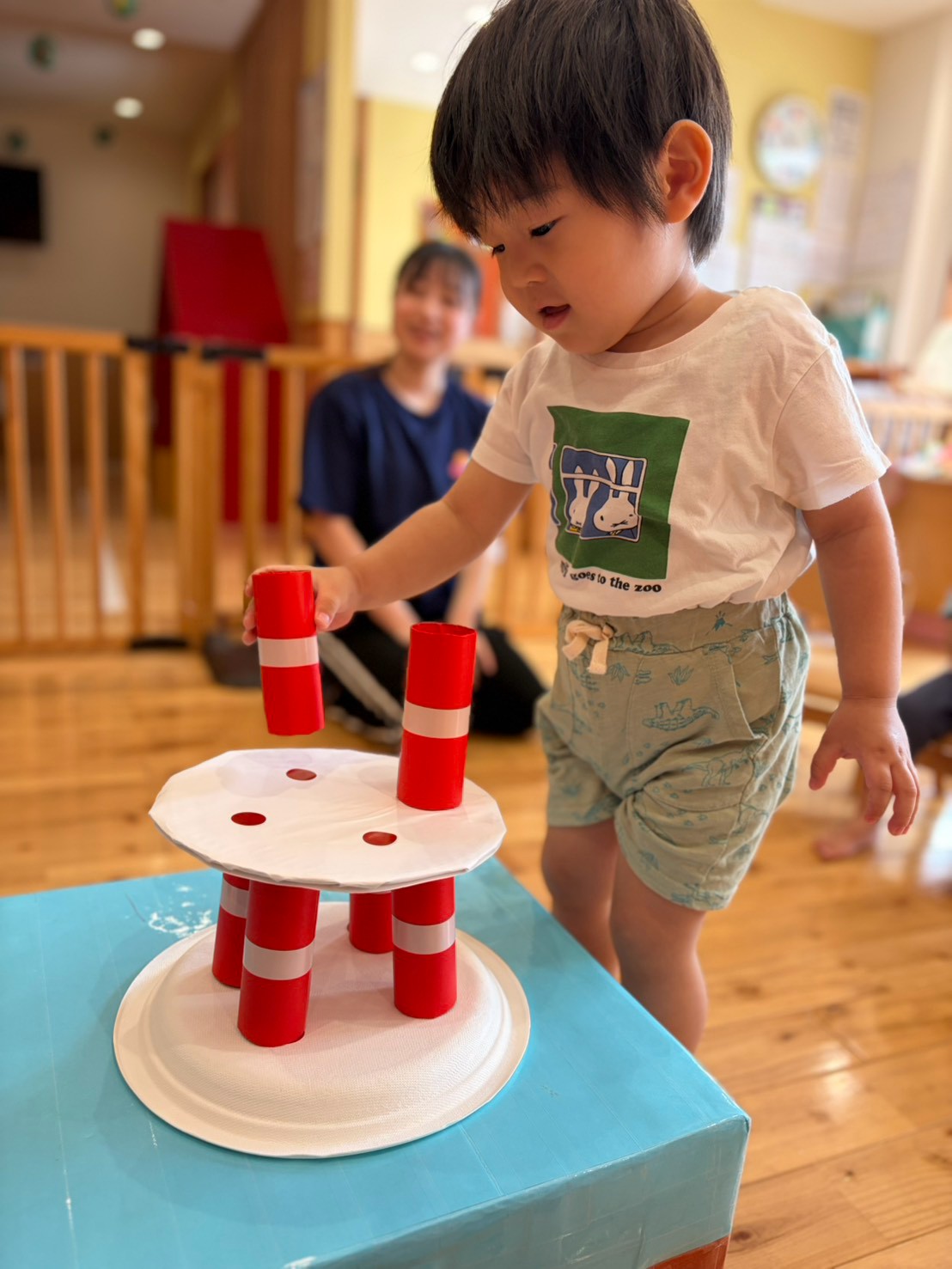 お誕生日会で赤い筒を上の段へ置こうとする子ども