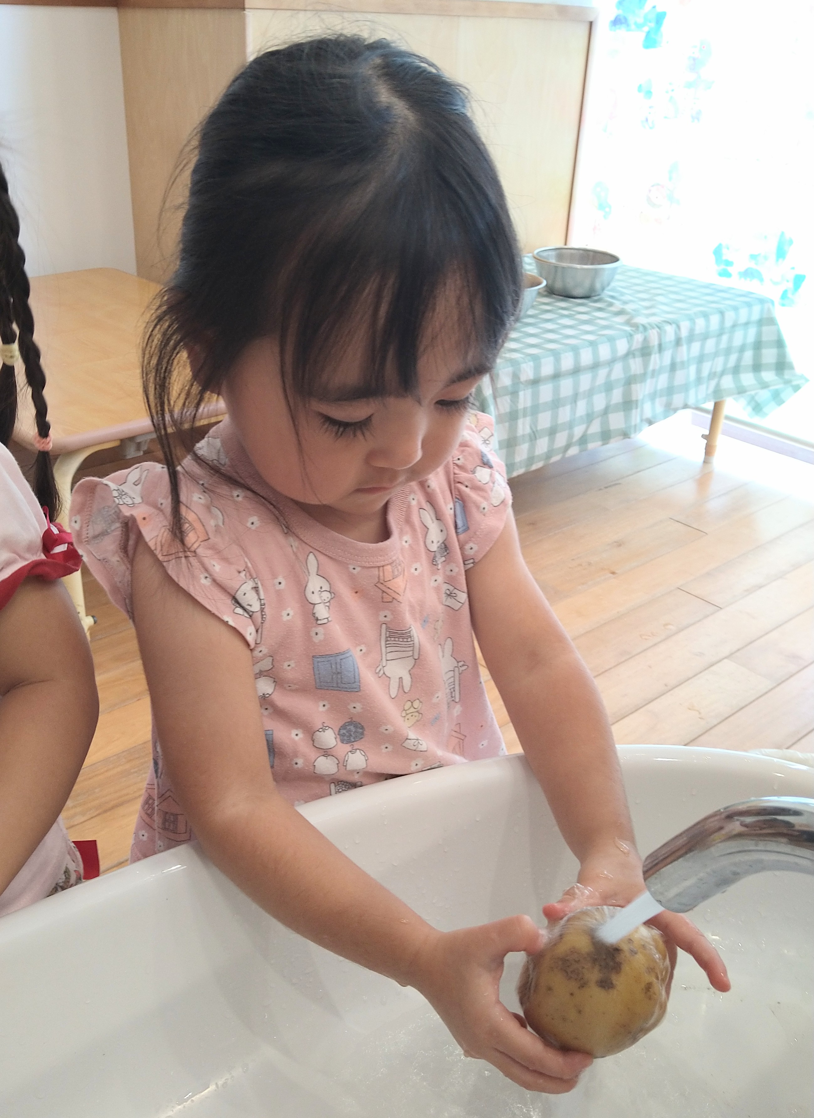 じゃがいもの汚れを見ながら水で洗う子ども
