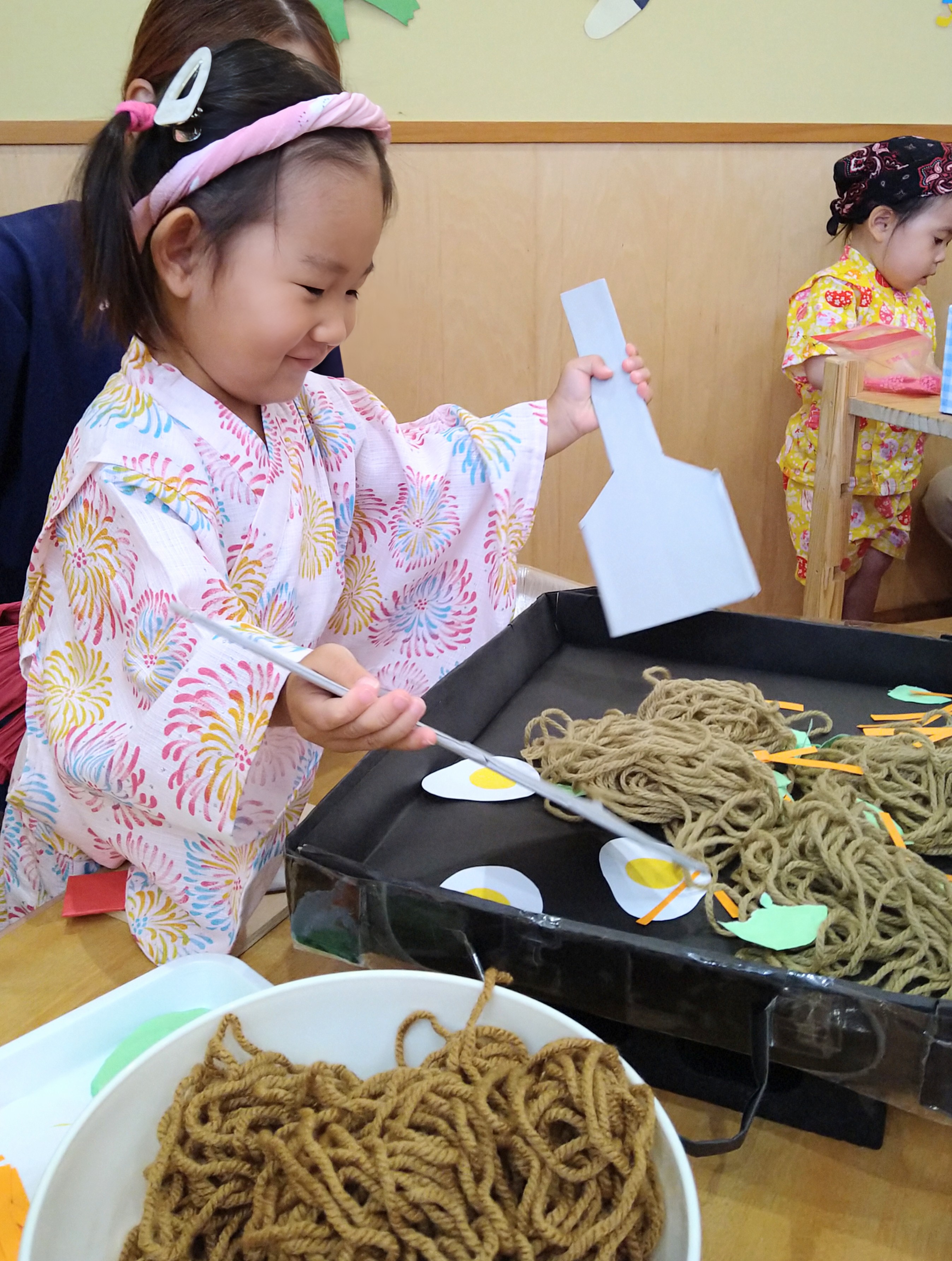 へらとトングを使って焼きそばに見立てた毛糸を盛り付ける様子