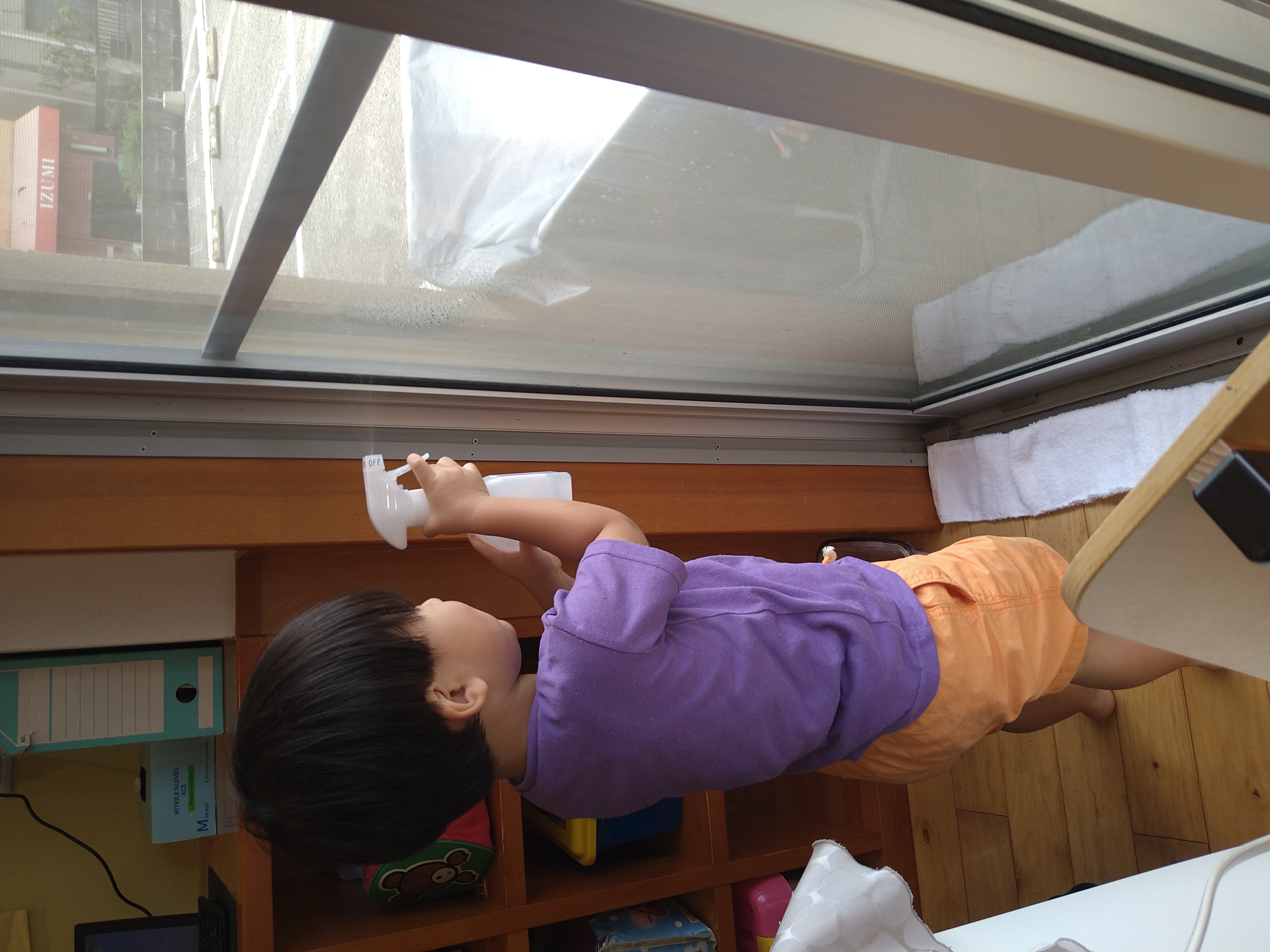 窓へ霧吹きを向けて両手で操作する子ども