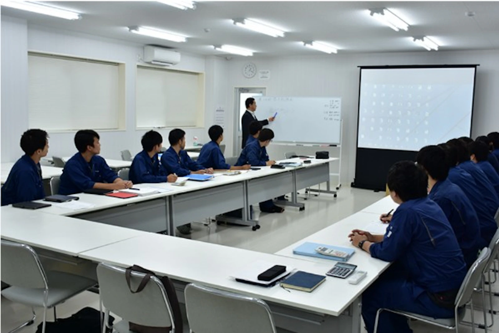 新卒社員向けの研修で、社長がホワイトボードの前で講義をする様子
