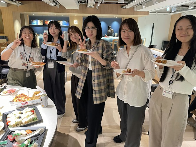 全社ミーティング後の懇親パーティーで料理を手に笑顔を見せる女性メンバーたち