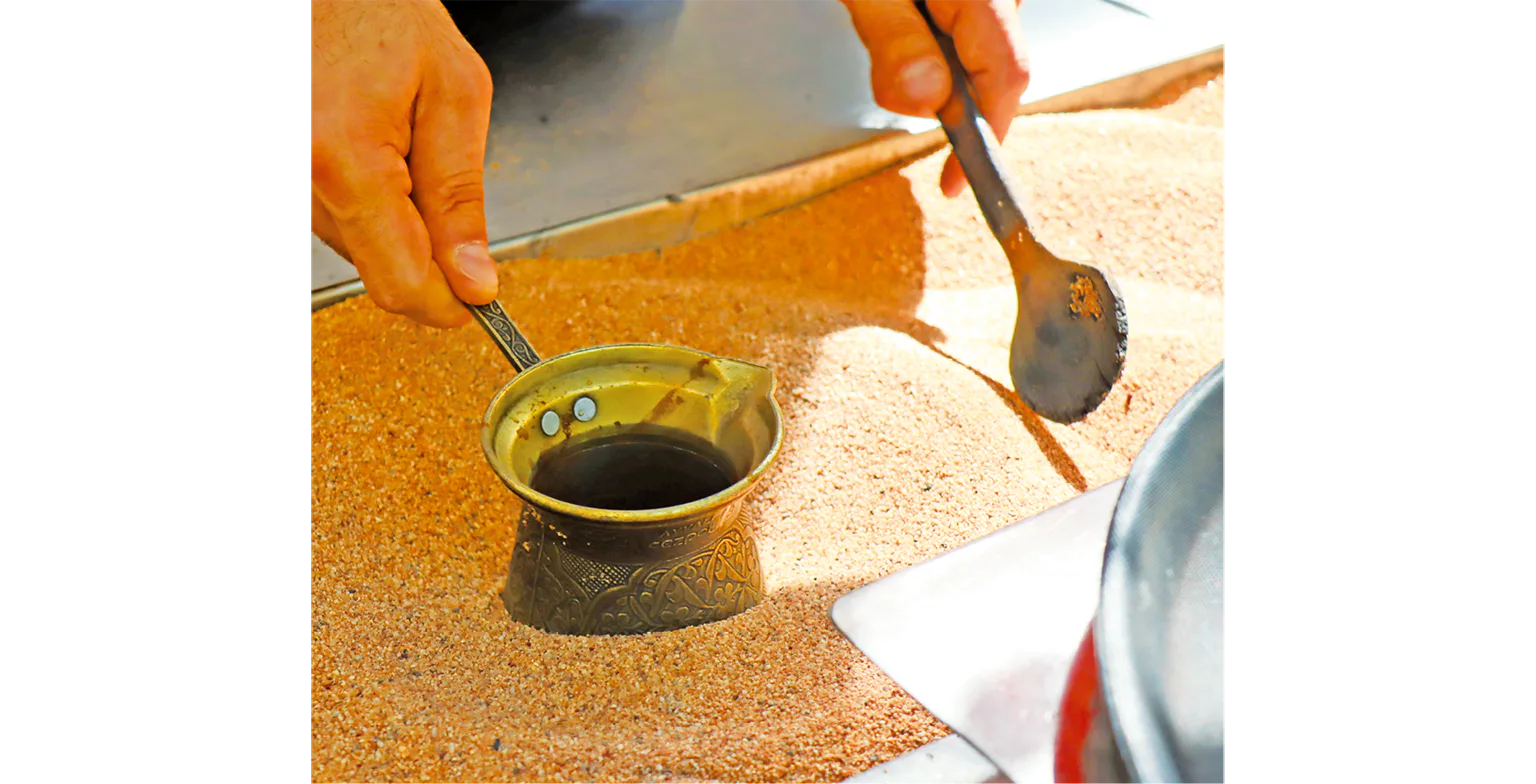 熱い砂にジェズヴェを埋め、ゆっくりと回しながら沸騰させてコーヒーを淹れるの画像
