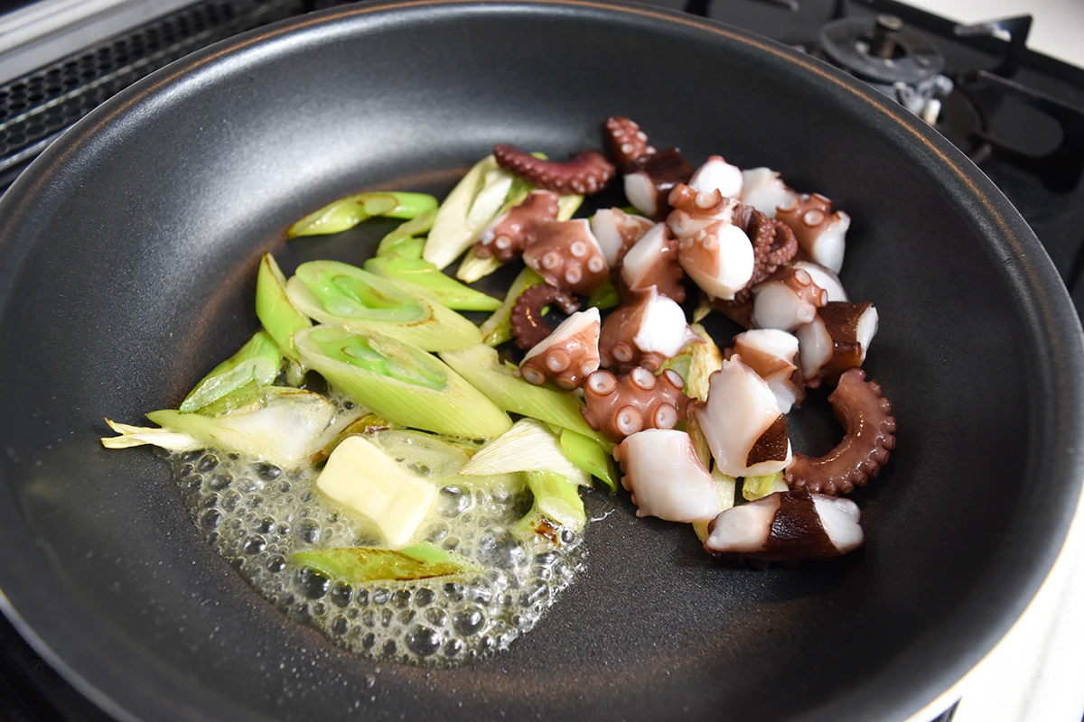 長ネギに色がついたらバターとタコを加える