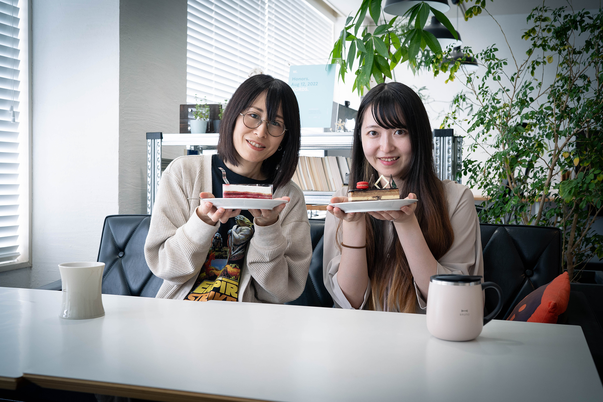 秋田オフィスのメンバー二人が、それぞれケーキを持って微笑んでいます。二人は白い皿にのったケーキを持っています。