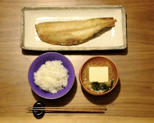写真:テーブルの上に、ご飯、みそ汁、焼き魚、箸が並べられている