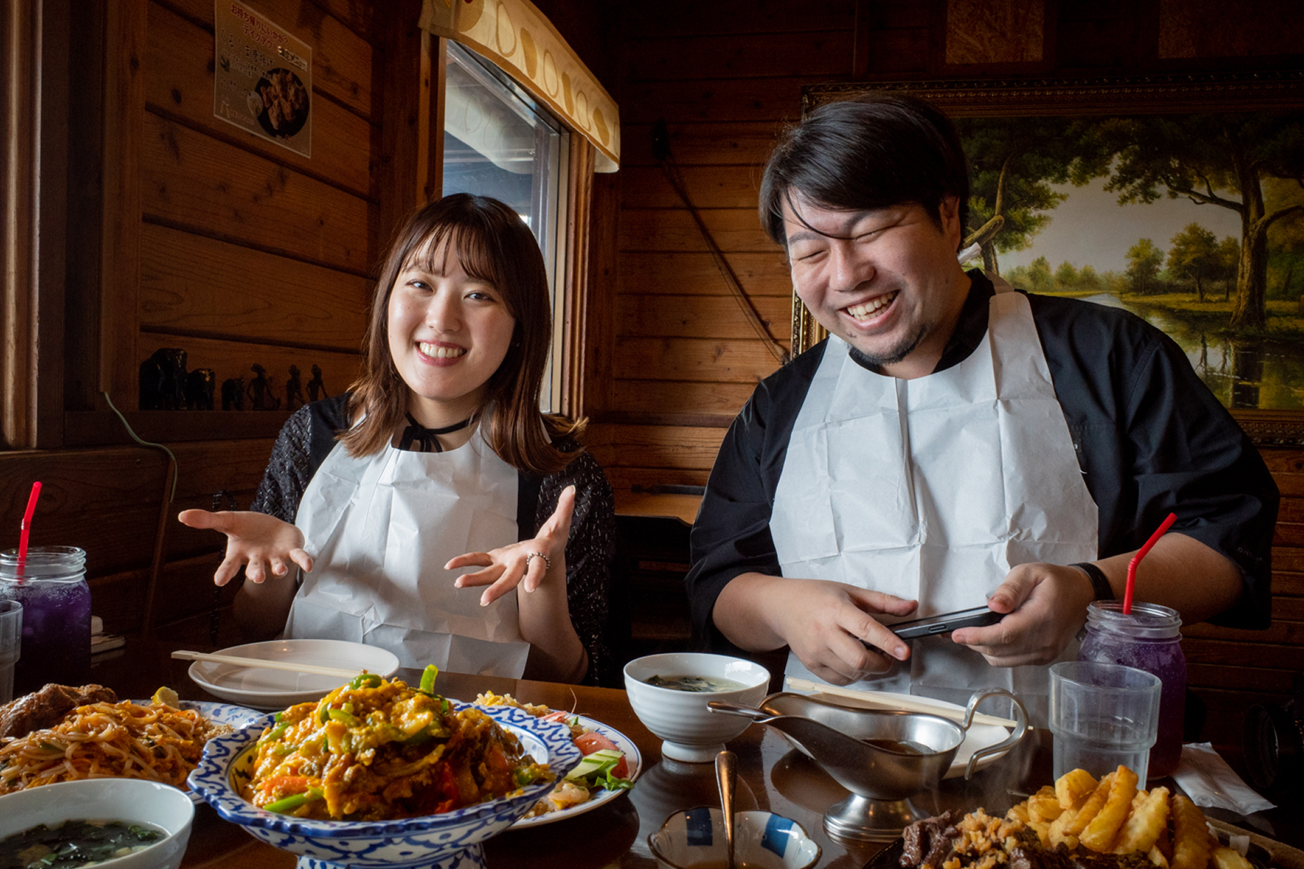 沖縄で美味しそうなご飯と一緒に写るデザイナーの中川さん(左)とCEOの阿部さん(右)